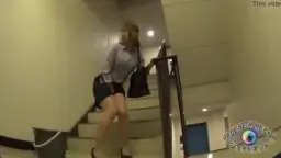 Asiatin in Hemdbluse hockt mit heruntergelassener Hose in weißem Treppenhaus und pinkelt