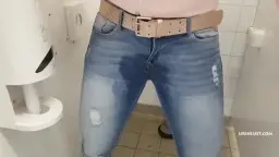 Blonde in Winterjacke lehnt wartend an der Toilettentür und schaut geil zur Seite